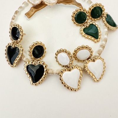 Brincos dourados com pedras em formas de coração e oval em preto, branco e verde sobre base cerâmica