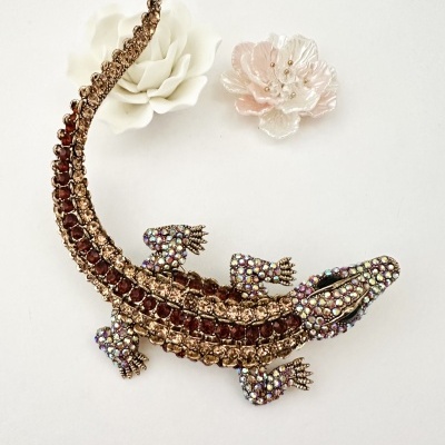 Broche em forma de crocodilo com cristais castanhos e iridescentes e duas flores artificiais branca e rosa