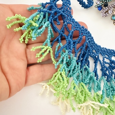 Colar colorido de contas de vidro azul, verde e branco com textura entrelaçada segurado por mão