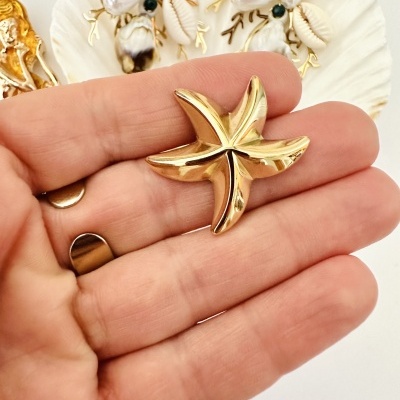 Peça em forma de estrela-do-mar dourada brilhante nas mãos com conchas ao fundo