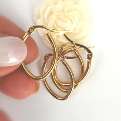 Conjunto de três brincos de argola dourados sobre fundo branco com flor decorativa creme