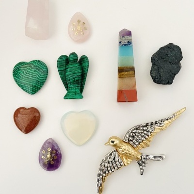 Pedras decorativas coloridas em várias formas e um broche de pássaro dourado e prateado sobre fundo branco