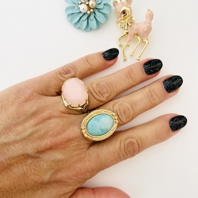 Anéis dourados com pedras coloridas e broches decorativos em fundo branco.