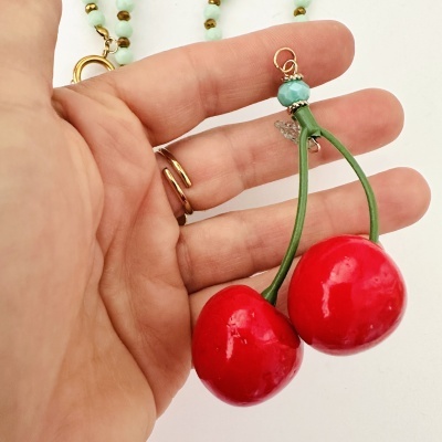 Colar com pingente de cerejas vermelhas e contas verdes em fundo branco
