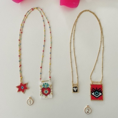 Dois colares de contas com pendentes coloridos e etiquetas numeradas sobre fundo claro com flores cor-de-rosa.