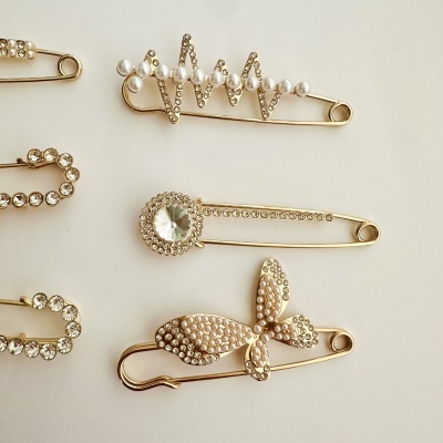 Alfinetes de segurança dourados com decoração de pérolas e pedras brilhantes