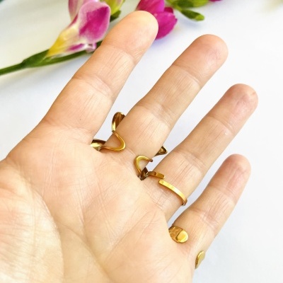 Mão com três anéis dourados e flores roxas e amarelas ao fundo