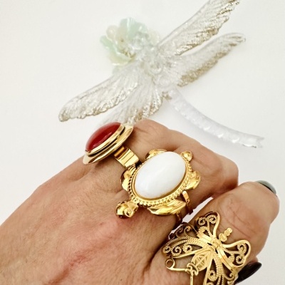 Mão com três anéis dourados e figura decorativa translúcida de libélula ao fundo