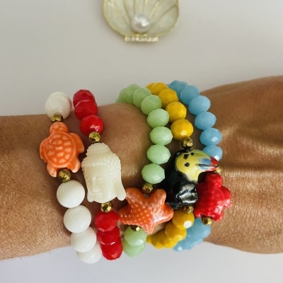Pulseiras coloridas com figuras em relevo num braço com concha decorativa na parede