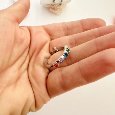 Brinco de argola prateado com pedras coloridas numa mão