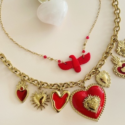 Colares dourados com pendentes vermelhos em forma de corações e um pá vermelho, dispondo sobre superfície branca.