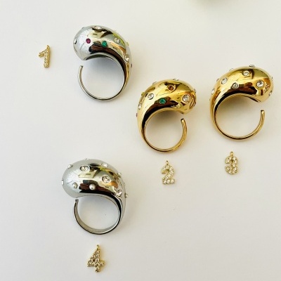 Cinco anéis dourados e prateados com pedras brilhantes e cinco números dourados soltos