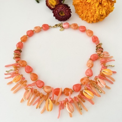 Colar com pedras e conchas laranja, fecho dourado, sobre fundo branco com flores secas.