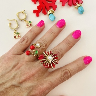 Anel floral dourado com pérola, brincos de cereja e brincos vermelhos com turquesa sobre fundo branco