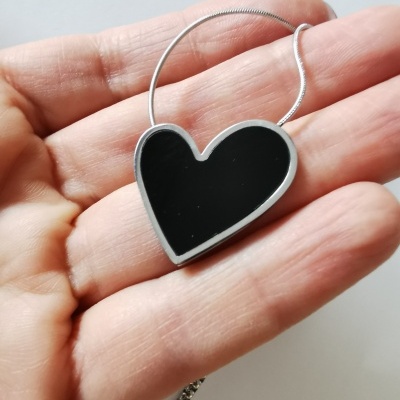 Colar coração preto com borda metálica numa mão