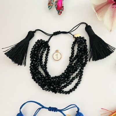 Bracelete de contas pretas com tassel preto e fecho ajustável num fundo branco com flor rosa e broche colorido