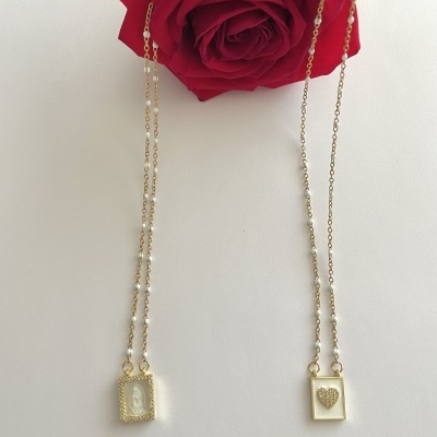 Colar dupla dourada com pingentes retangulares e rosa vermelha atrás