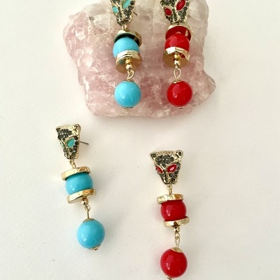 Quatro brincos pendentes com contas em azul e vermelho sobre fundo branco e uma pedra rosa