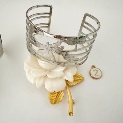 Pulseira prateada com libélulas sobre flor branca decorativa