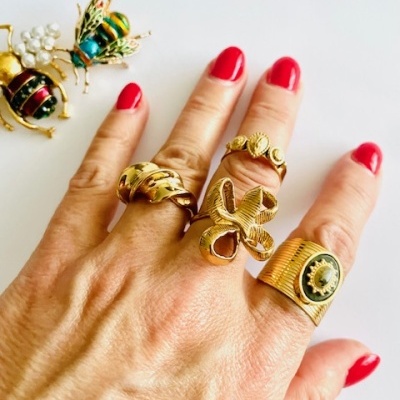 Mão com anéis dourados e uns broches de abelhas coloridas junto