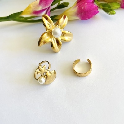 Três anéis dourados com pérolas e flores coloridas ao fundo
