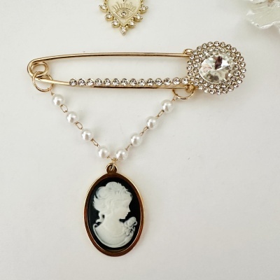 Alfinete dourado com pedras e pendente oval com relevo feminino
