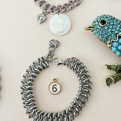 Braceletes de corrente prateada com pendentes e figura de pássaro colorida à direita