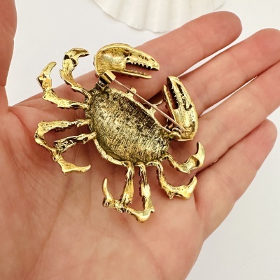 Broche dourado em forma de caranguejo na palma da mão