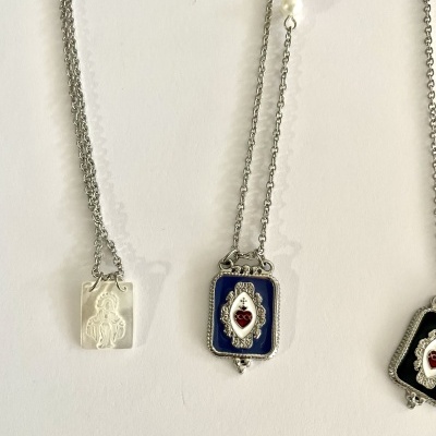 Colares com pingentes religiosos prateados com detalhes em branco, azul e vermelho