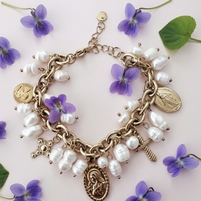 Pulseira dourada decorada com pérolas e medalhões, rodeada por flores roxas