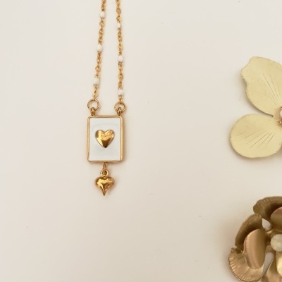 Colar dourado com pingente retangular branco e corações dourados ao lado de flores decorativas