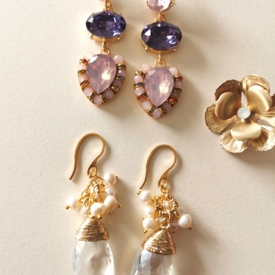 Três pares de brincos com pedras coloridas, pérolas e detalhes dourados sobre fundo claro.