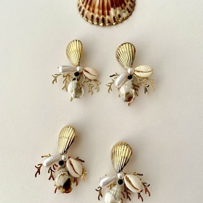 Quatro pares de brincos com motivos marinhos e uma concha natural sobre fundo branco