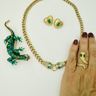 Conjunto de joias ouro com pedras verdes e brancas sobre fundo branco.