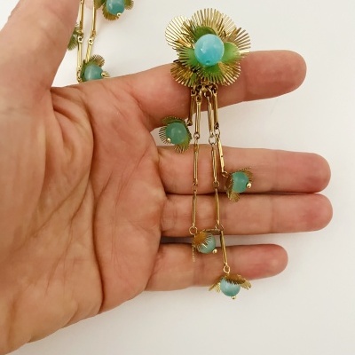 Brincos dourados com pedras verdes em forma de flor e detalhes pendentes