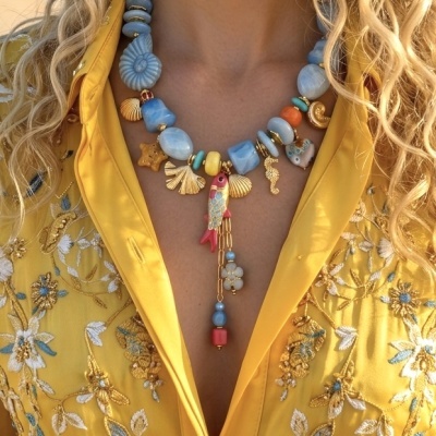 Colar colorido com contas grandes e pendentes marinhos, camisa amarela bordada com flores