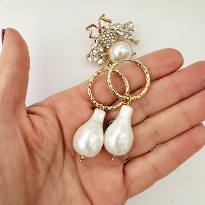 Brincos de pérola e cristais em formato de abelha sobre mão