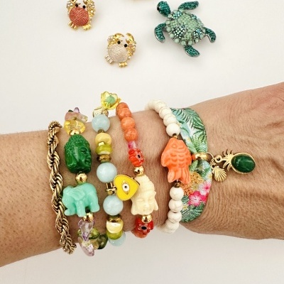 Pulseiras coloridas e pins de animais com strass em fundo branco.