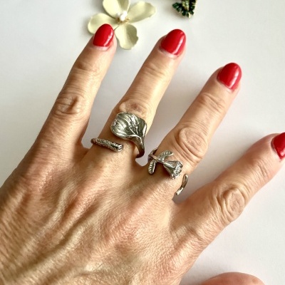 Mão feminina com anéis prateados e unhas vermelhas junto a flor e pendente colorido