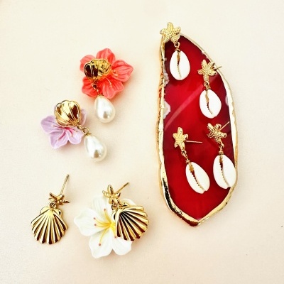 Brincos coloridos com flores, pérolas, conchas e estrela-do-mar sobre base vermelha com borda dourada