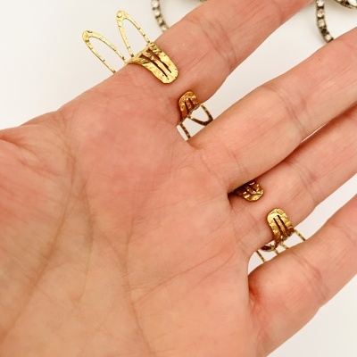 Anel dourado num dedo com peças de bijuteria em forma de flores com cristais no fundo