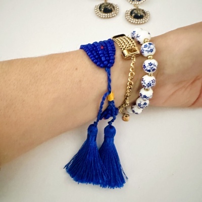Pulso com três pulseiras em azul, dourado e branco com padrões florais em fundo branco