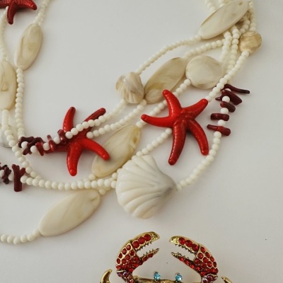 Colar branco com estrelas do mar vermelhas e broche de caranguejo dourado com pedras vermelhas e azuis