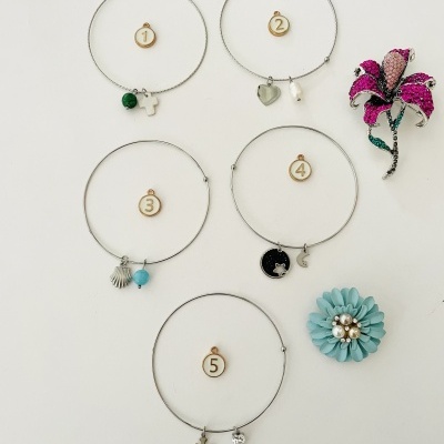 Cinco pulseiras metálicas com pendentes e dois broches florais coloridos em fundo branco