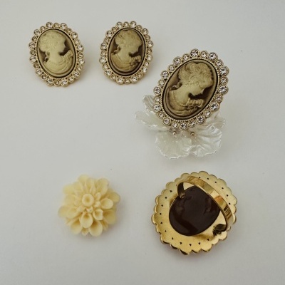 bijuterias com camafeu dourado e flor creme sobre fundo branco