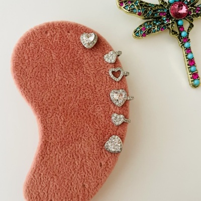 Brincos prateados com pedras brilhantes em base rosa felpuda ao lado de broche libélula colorido.