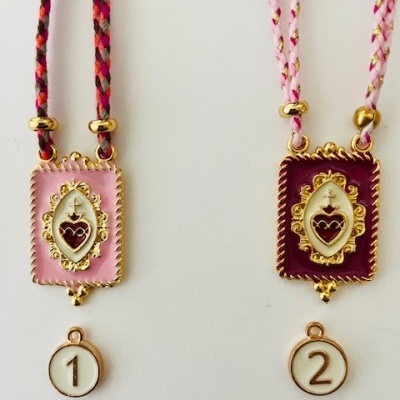 Dois colares com placas retangulares decorativas e medalhas numeradas penduradas em cordões trançados coloridos.