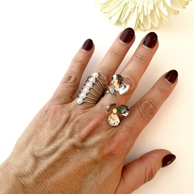 Mão com anéis prateados e unhas castanhas ao lado de flor branca