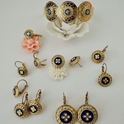 Conjunto de joias douradas com detalhes azuis e verdes sobre flores artificiais.