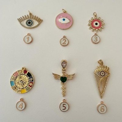 Seis pendentes dourados numerados com designs variados e olhos estilizados em fundo branco